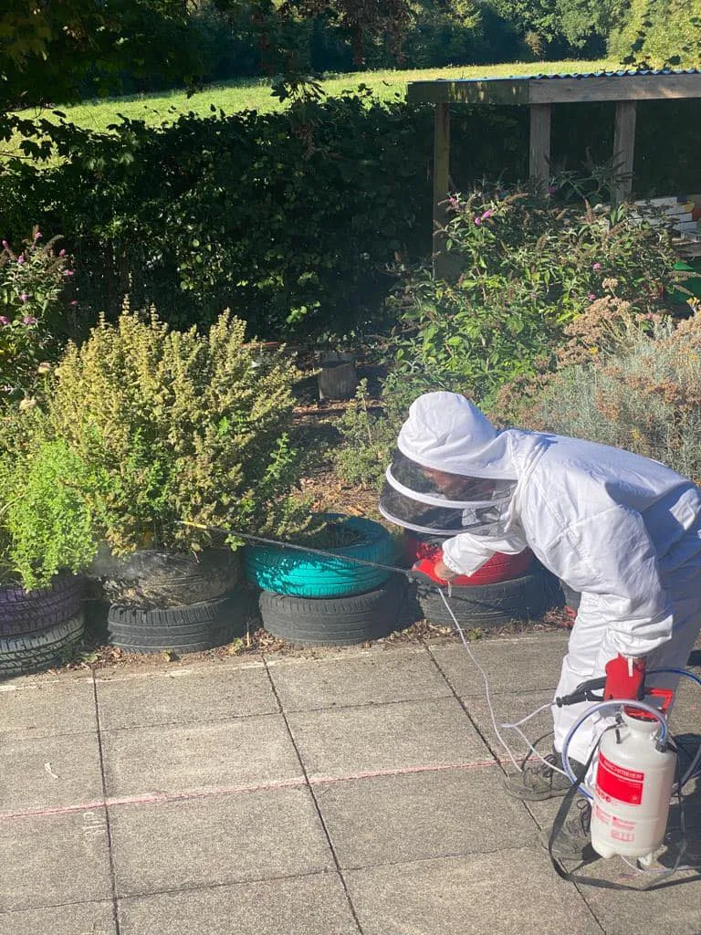 A man in a white suit spraying a garden.
